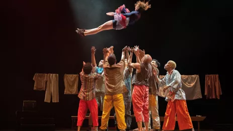 Woman mid-air with small crowd waiting to catch her underneath on stage