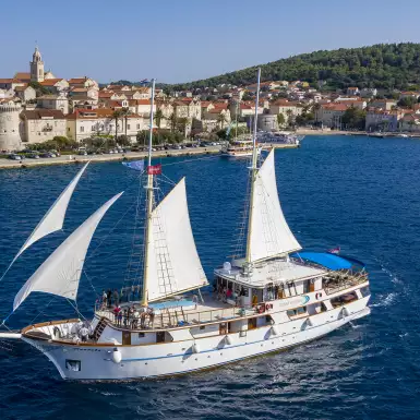 MS Mendula sailing with sails up, coastline in the background